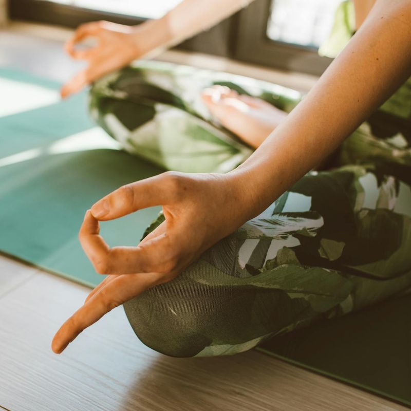 Close-up of a person's hands in a meditative pose on a yoga mat.